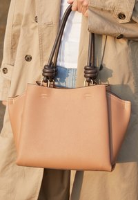 Sac à main en cuir grainé marron avec un design structuré, des poignées doubles nouées et des coutures blanches contrastantes.