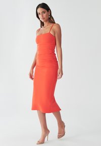 Figurbetontes, knielanges Kleid aus leuchtend orangefarbenem Stoff mit Raffung, dünnen Trägern und leicht ausgestellt am Saum.