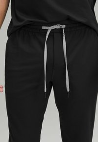 Sorte joggingbukser med elastik i livet og en grå snor. Stoffet er glat med en let glans og har et minimalistisk design.