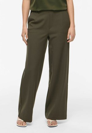 Femme portant un pantalon large vert olive et un haut sans manches assorti, associé à des sandales blanches en tongs.