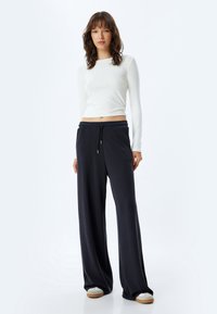 Witte lange mouwen top met een slim fit, gecombineerd met losse donkerblauwe broek met een elastische tailleband en trekkoord.