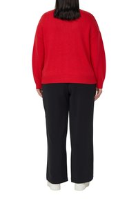 Rode gebreide trui met een ontspannen pasvorm, geribbelde zoom en boorden, gecombineerd met zwarte broek met wijde pijpen en witte sneakers. Achteraanzicht getoond.