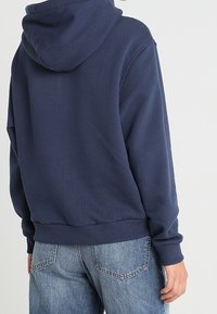 Navy blue hooded sweatshirt with a relaxed fit, ribbed cuffs and hem, soft fabric texture. Featured back view, highlighting its simplicity.