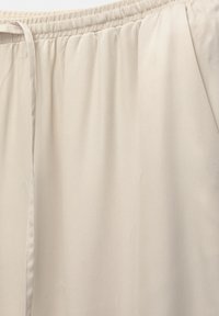 Ljusbeige byxor med elastisk midja, i mjukt och slätt tyg med diskreta veck för extra struktur och komfort.