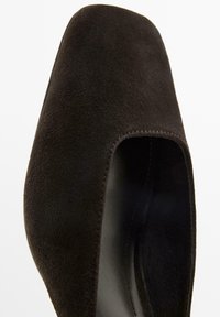 Black suede high-heeled shoe with a rounded toe and a cut-out detail on the sides. Smooth inner lining and subtle stitching accents.