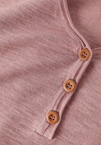 Tessuto a maglia rosa chiaro con tre bottoni in legno lungo una patta, con una consistenza morbida e una leggera lucentezza data dal filato.