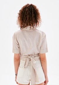 Chemise courte à manches courtes beige clair avec col, nouée à la taille avec une ceinture assortie, assortie à un pantalon court de couleur crème. Texture douce.