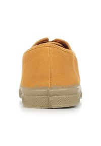 Baskets slip-on en toile beige avec bout rond, semelle en caoutchouc plate et détails de couture. Le design présente une texture lisse sans quincaillerie visible.