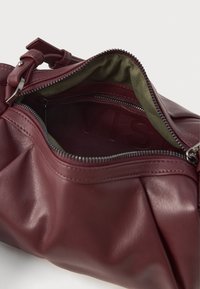 Sac en cuir bourgogne avec une ouverture zippée, présentant une texture douce et une doublure en tissu vert. Contient un logo de marque embossé à l'intérieur.