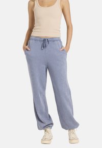 Jasnoniebieskie bawełniane spodnie dresowe z elastycznym pasem, bocznymi kieszeniami i luźnym krojem, w połączeniu z beżowym topem na ramiączkach i beżowymi trampkami.