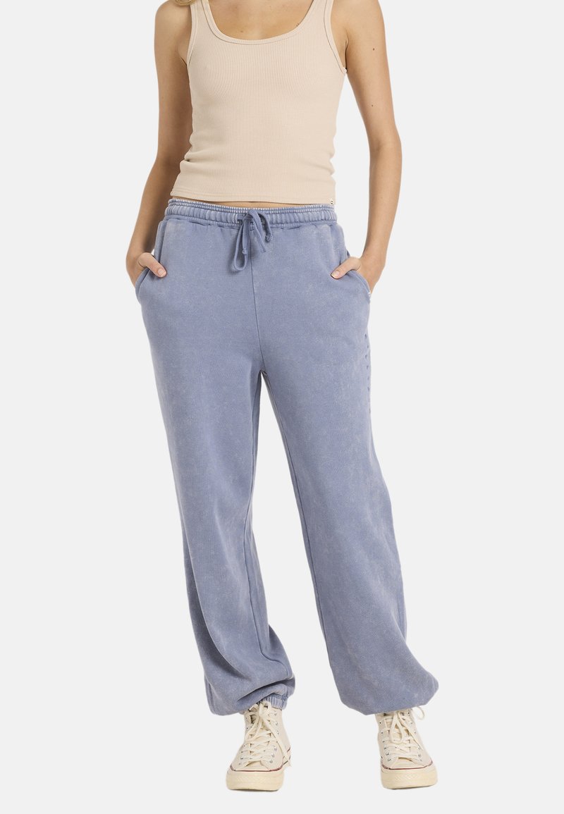 Jasnoniebieskie bawełniane spodnie dresowe z elastycznym pasem, bocznymi kieszeniami i luźnym krojem, w połączeniu z beżowym topem na ramiączkach i beżowymi trampkami.