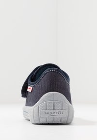 Navy textile shoe with a Velcro strap, gray rubber sole, and contrasting stitching. Features a small branded tag on the side.