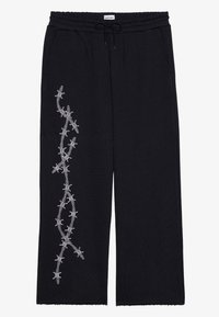 Zwarte sweatpants met een elastische tailleband, trekkoord, zijzakken en witte geborduurde prikkeldraad langs het linkergewricht. Zachte stof textuur.