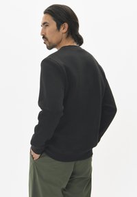 Zwarte sweater met een ronde hals en lange mouwen, gemaakt van een zacht materiaal. Draag het met olijfgroene broeken.