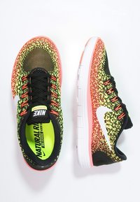 Běžecké boty Nike s pleteným svrškem v černé, žluté a růžové barvě, obsahující bílé logo swoosh, černé šňůrky a polstrovanou bílou podrážku.