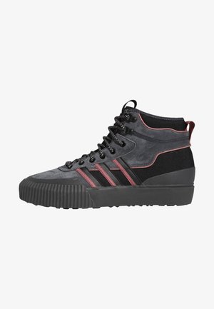 Deportivas de caña alta en ante negro y gris con acentos rojos. Presentan una suela de goma texturizada y cordones en la parte delantera con ojales de metal.
