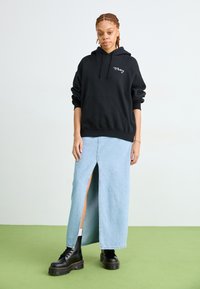 Črna kapuca z logotipom "obey", v kombinaciji s svetlo modrim denim maxi krilom z režo spredaj, obuta v črne platforme s čipkami.