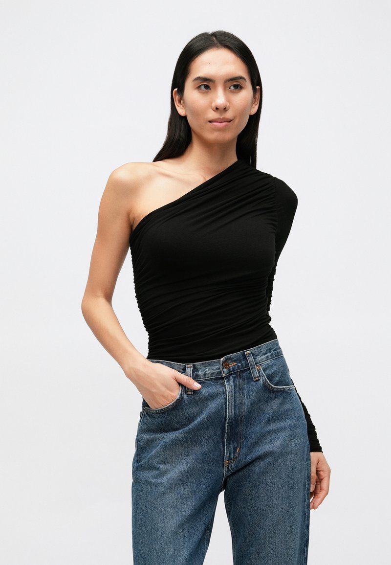 Haut noir asymétrique avec tissu froncé, associé à un jean en denim bleu taille haute. Texture lisse et coupe ajustée qui souligne la silhouette.