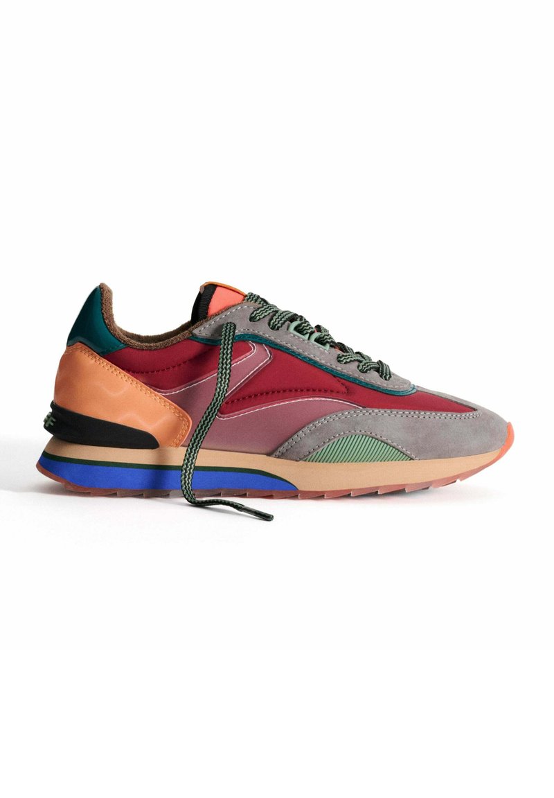 Zapatilla multicolor con una mezcla de materiales grises, burdeos y naranjas, con un diseño texturizado, cordones verdes y un acento azul en la suela.