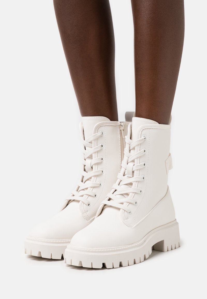 Weiße Leder-Stiefeletten mit einer dicken Sohle, Schnürung vorne und Reißverschluss an der Seite; mit einer strukturierten Oberfläche und einer Schlaufe hinten.