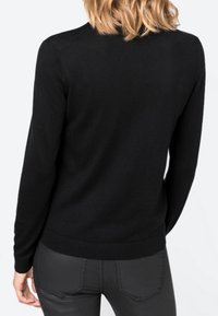 Svart stickad tröja med långa ärmar, med rund halsringning och ribbad nederkant, bärs över mörka, åtsittande byxor. Slät textur, enkel design.