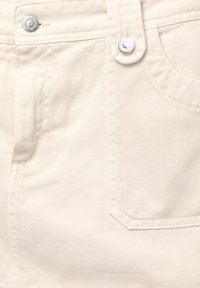 Tissu en denim beige avec une texture détaillée, comportant un bouton en métal et une poche avant. Couture visible le long des coutures.