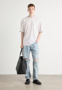 Lyslilla oversized t-shirt med broderet logo, slidte lyseblå jeans, sort tote bag og sorte sko. Minimalistisk design, afslappet pasform.
