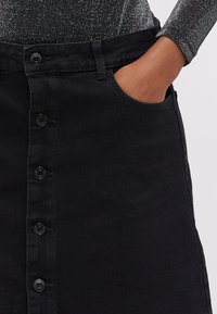 Črna denim krilo z visokim pasom, sprednjim zapiranjem na gumb in stranskimi žepi. Tkanina ima gladko teksturo in rahlo elastičnost.