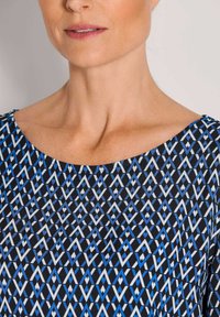 Black dress featuring a geometric blue and white pattern, with a wide neckline and smooth, textured fabric. Neck and shoulders visible.