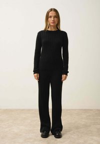 Pull en tricot noir côtelé et pantalon assorti, avec un col rond et des manches longues. Texture douce, coupe décontractée, porté avec des chaussures plates.