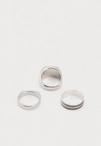 Tres anillos de plata sobre una superficie blanca: dos con cúpulas lisas y planas y uno con dos diseños de cuerda negra retorcida alrededor de la banda.