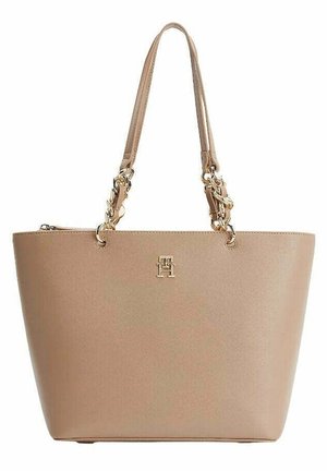 Beige läderhandväska med dubbla axelremmar som har guldkedjelänkar och en liten guld "TH"-logotyp på framsidan.