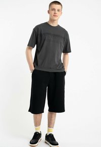 Szary t-shirt z krótkim rękawem z delikatnym wytłoczonym napisem, w połączeniu z luźnymi czarnymi szortami, czarnymi trampkami i skarpetkami w żółte paski.