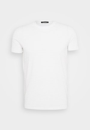 T-shirt blanc à manches courtes et col ras du cou avec une texture en relief subtile de nom de marque répétée, présentée sur un fond gris clair uni.