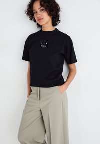 Zwarte katoenen t-shirt met korte mouwen, een ronde halslijn en witte bedrukte tekst met de woorden "CPH STUDIOS" gecentreerd op de voorkant.