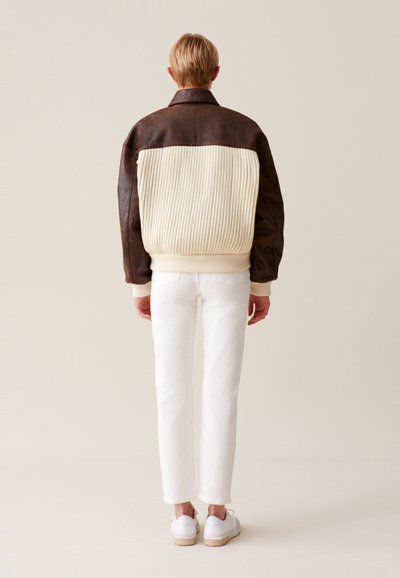 Hnedá kožená bunda s krémovou rebrovanou tkaninou a vysokým golierom, skombinovaná s bielymi priliehavými nohavicami a bielymi teniskami. Jednoduchý dizajn, bez vzorov.