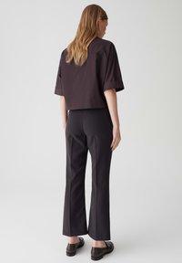 Haut noir cropped à manches courtes, associé à un pantalon noir moulant légèrement évasé, avec une texture lisse et un design minimaliste.
