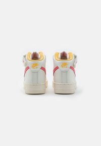 Nike Air sneakers med ovandel i vitt läder, rosa accentrand, gul krage och texturerad gummisula. Har varumärkeslogotyp på hälen.