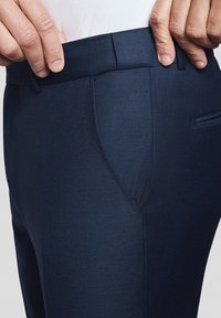 Granatowe spodnie wykonane z teksturowanej tkaniny, z prostym przodem, kieszeniami bocznymi i gładkim pasem w talii. Zbliżenie na obszar pasa.