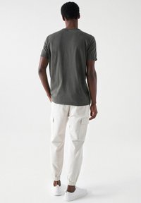 Olivgrünes T-Shirt kombiniert mit cremefarbenen Cargohosen mit elastischen Bündchen und seitlichen Taschen, ergänzt durch weiße Sneaker.