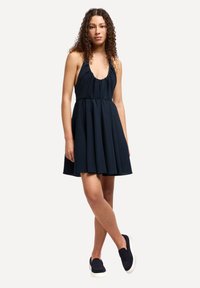 Abito a halter blu navy con vita arricciata e gonna svasata; realizzato in tessuto morbido. Abbinato a scarpe nere slip-on per un look informale.