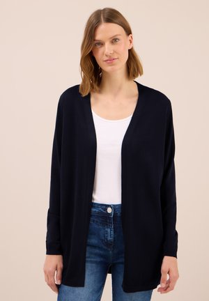 Navy cardigan with open front, long sleeves, and a relaxed fit, worn over a white top, paired with blue jeans. Soft knit texture.