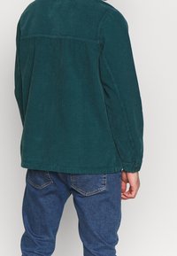 Teal kordflorskjorta med knapp-down krage, långa ärmar och en vertikal ribbad textur. Kombinerad med blå denimjeans.