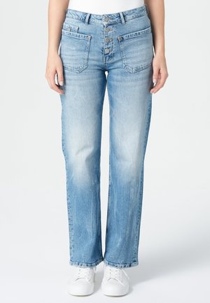 Person trägt hellblaue Jeans mit geradem Bein, Knopfverschluss und großen vorderen Taschen, kombiniert mit weißen Sneakers.