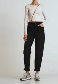 Top corto de manga larga blanco con textura de canalé y detalles de botones, combinado con unos vaqueros negros holgados de cintura alta y zapatillas grises con cordones blancos.