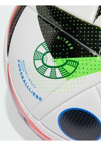 Biela futbalová lopta s čiernymi a zelenými akcentmi, obsahujúca modré a čierne bodky a tlačené dizajnové prvky. Text obsahuje "REPLIKA ZÁPASNÉ LOPTY."