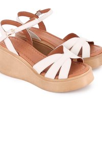 Sandalias de cuña de piel blanca con tiras entrelazadas, plantilla color marrón y suela de plataforma beige. Presentan un cierre de hebilla en la correa del tobillo.