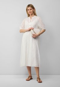 Vestido midi blanco con tejido transparente y un patrón de hojas texturizado, con un frente abotonado y mangas abullonadas, combinado con sandalias marrones.