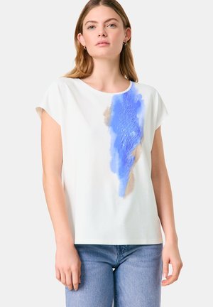 White short-sleeve top featuring blue and beige abstract paint designs. Made of smooth fabric, with a relaxed fit and round neckline.