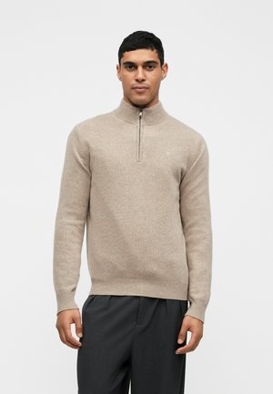Beige, zip-neksweater van zacht materiaal. Beschikt over lange mouwen en geribbelde manchetten en zoom. Minimalistisch ontwerp met een subtiele logo-detail.